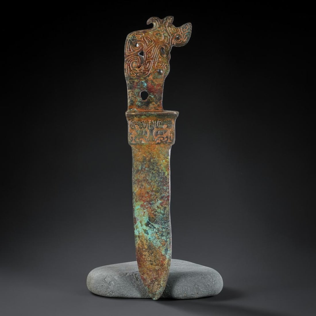 A Chinese Archaic-Style Bronze Dagger With Openwork Pommel, 63AD: Cast in bronze, this ceremonial dagger features an elaborate openwork pommel decorated with stylized beast-mask and scroll motifs with multiple piercing holes. The hilt collar carries a continuous ban