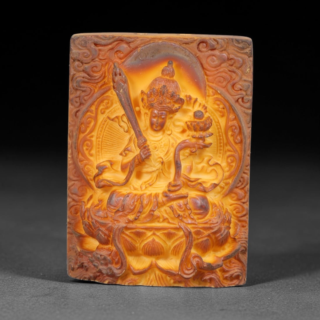 A Chinese Manjushri Deity Carved Tagua Nut Pendant Amulet, 87BC: Carved from tagua nut, this rectangular tablet-form amulet is worked in high relief. Manjushri is depicted seated in partial lotus posture upon an ornate lotus pedestal, holding the flaming wisdom swo