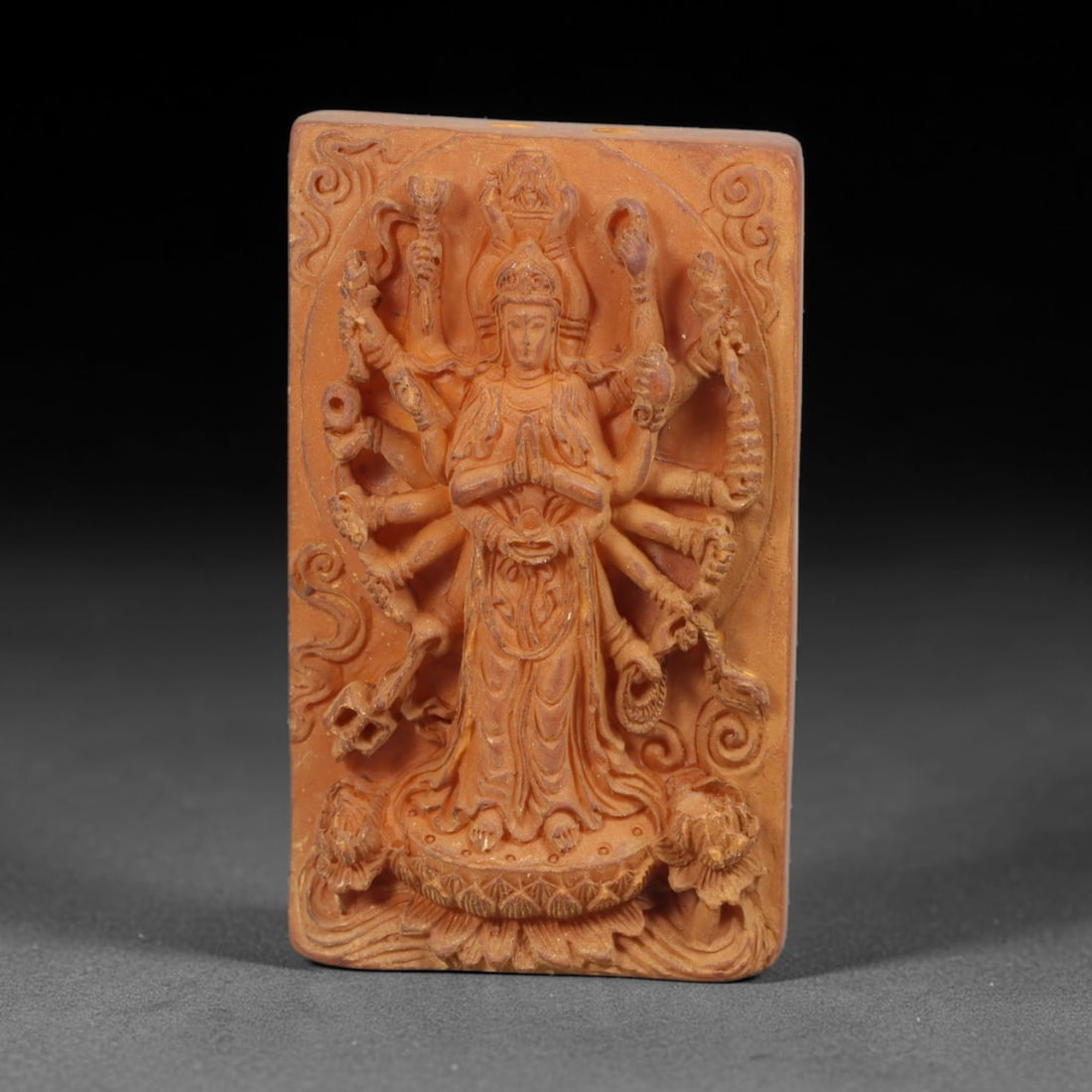 A Chinese Multi-Armed Guanyin Deity Carved Tagua Nut Pendant Amulet, 97BC: Carved from tagua nut, this rectangular tablet-form amulet is executed in high relief. The central figure depicts multi-armed Guanyin standing upon a detailed lotus pedestal, primary hands joined in a