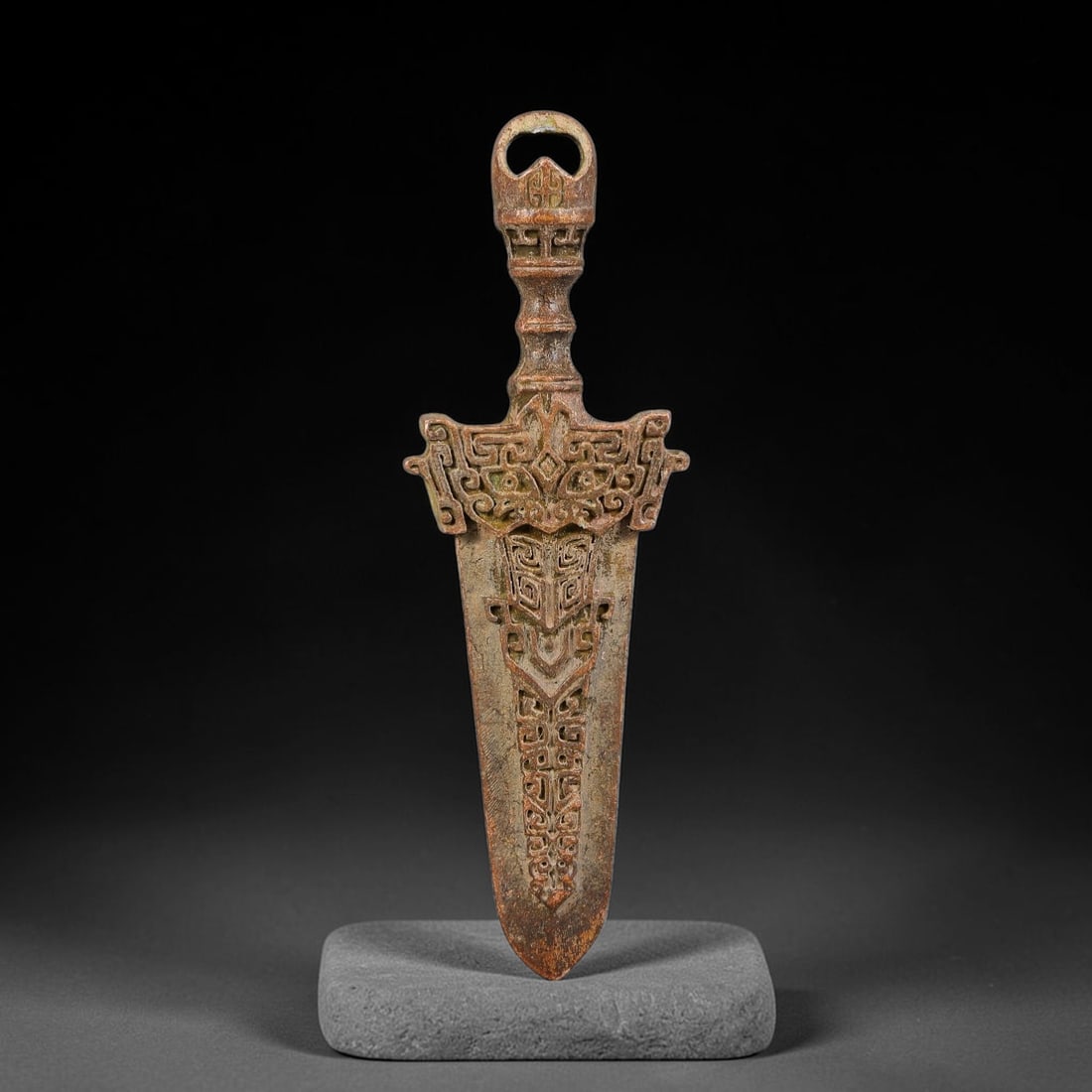 A Chinese Bronze Archaic-Style Dagger Amulet, 18AD: Cast in bronze, this flat dagger-form amulet features a suspension loop at the pommel for attachment. The hilt and blade face are densely decorated with deeply-cast archaic scroll and stylized beast-m