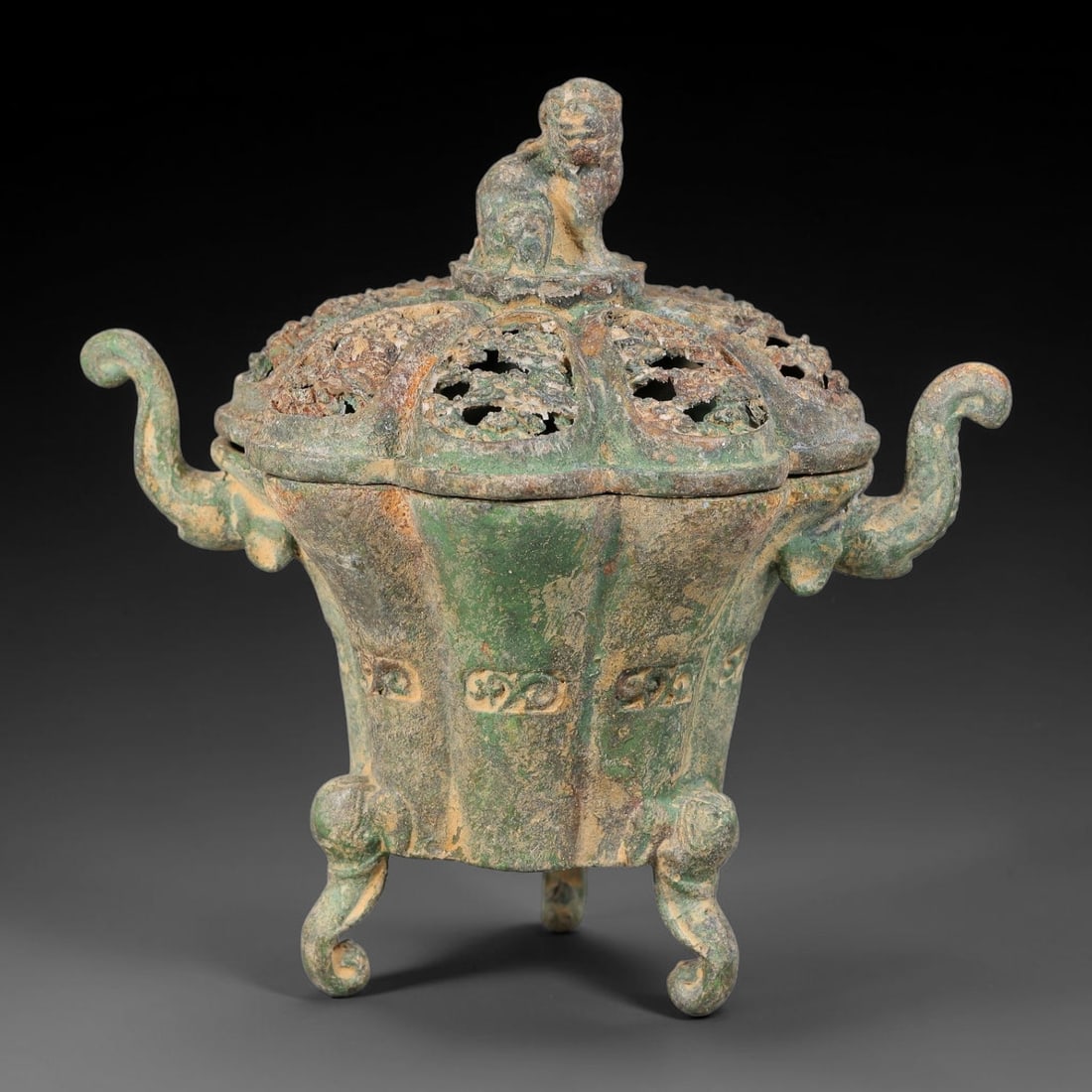 A Chinese Bronze Lion-Finial Tripod Censer, 67AD: Cast in bronze, this tripod censer possesses a lobed body adorned with low-relief archaic scroll motifs. Its pierced openwork lid is surmounted by a seated guardian lion finial, allowing incense smoke