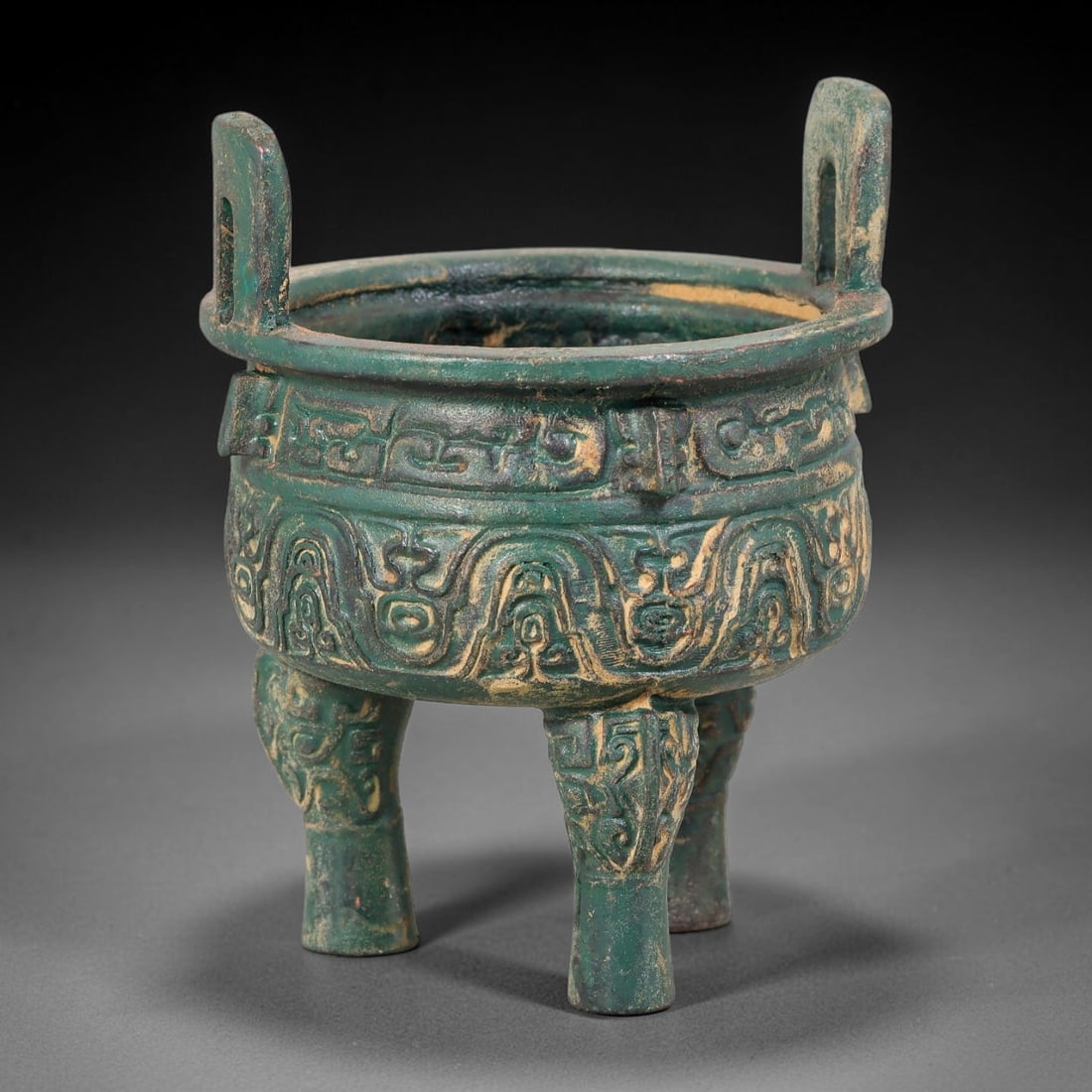 A Chinese Archaic-Style Bronze Tripod Ding Vessel, 73AD: Cast in bronze, this miniature tripod ding vessel features upright rectangular loop handles rising from the broad rim. The rounded bulbous body is decorated in relief with layered archaic scroll and s