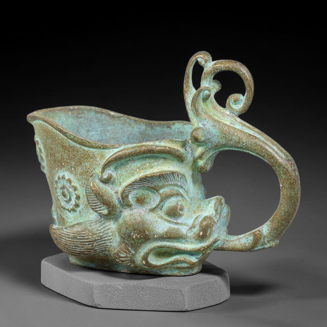 A Chinese Archaic-Style Bronze Dragon-Head Libation Cup, 76AD: Cast bronze libation cup with prominent three-dimensional dragon-head forming the front wall, complete with detailed eyes, nostrils and whiskers. An elaborate scrolling open-work dragon-form handle ex