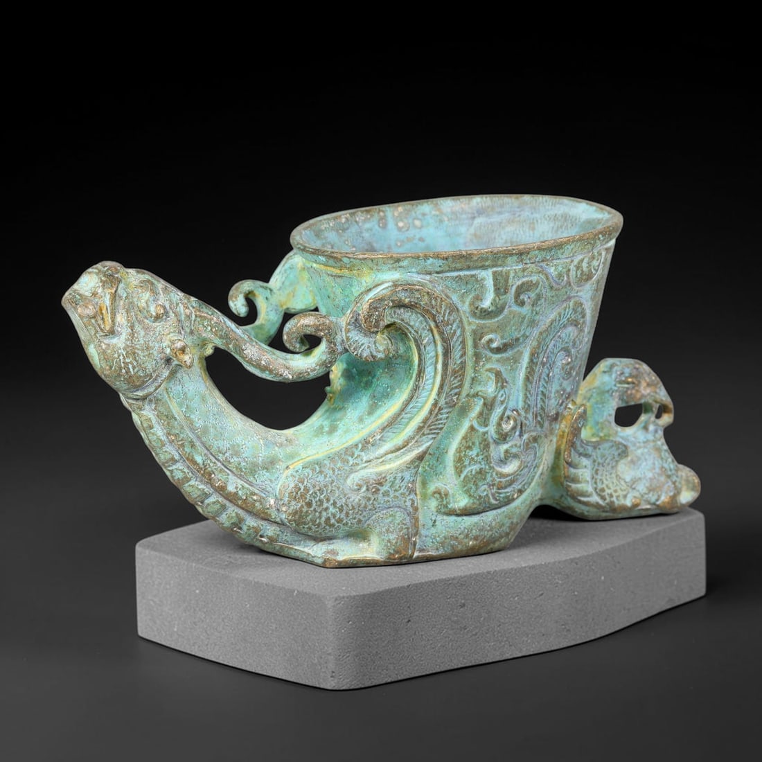 A Chinese Archaic-Style Bronze Dragon-Form Rhyton Libation Cup, 11AJ: Cast bronze rhyton-form libation vessel with a prominent dragon-head spout extending forward, its scaled body forming the base, with a small open-work phoenix-form tail terminal at the rear. The cup b