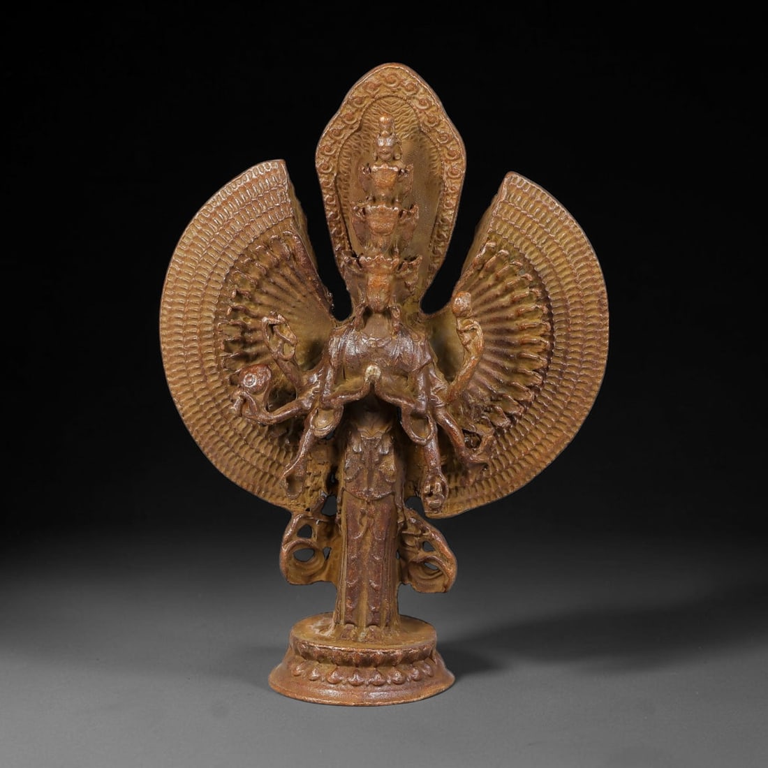 A Chinese Bronze Thousand-Armed Avalokitesvara Figure, 87AD: Cast bronze standing figure of Thousand-Armed Avalokitesvara, with multi-tiered stacked heads and expansive fan-shaped thousand-armed mandorla behind the main body. Multiple primary hands hold varied 