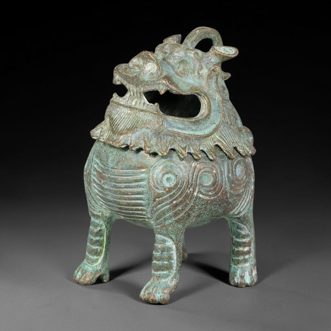 A Chinese Bronze Mythical Beast-Form Luduan Censer, 85AD: Cast bronze censer modelled as a luduan mythical beast, with detachable head-form lid; open-mouthed head functions as smoke outlet. The rounded body is decorated with incised spiral and horizontal rib