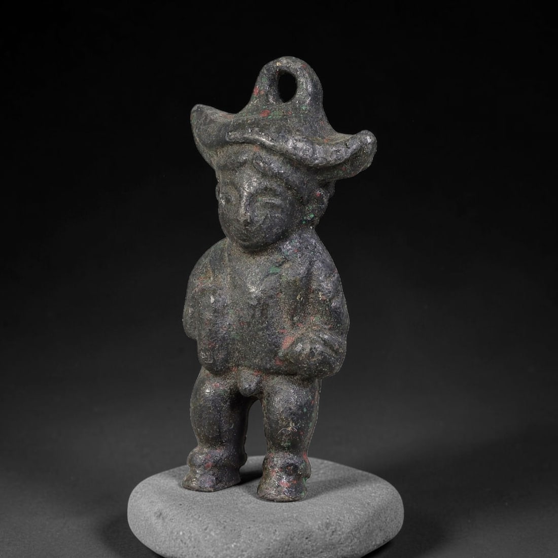 A Chinese Bronze Standing Pendant Figurine with Broad Brimmed Headdress, 45AD: Cast bronze standing figurine with integrated suspension loop rising from its wide-brimmed headdress. The figure displays stylized facial features and simple modelled clothing, with hands held at the 