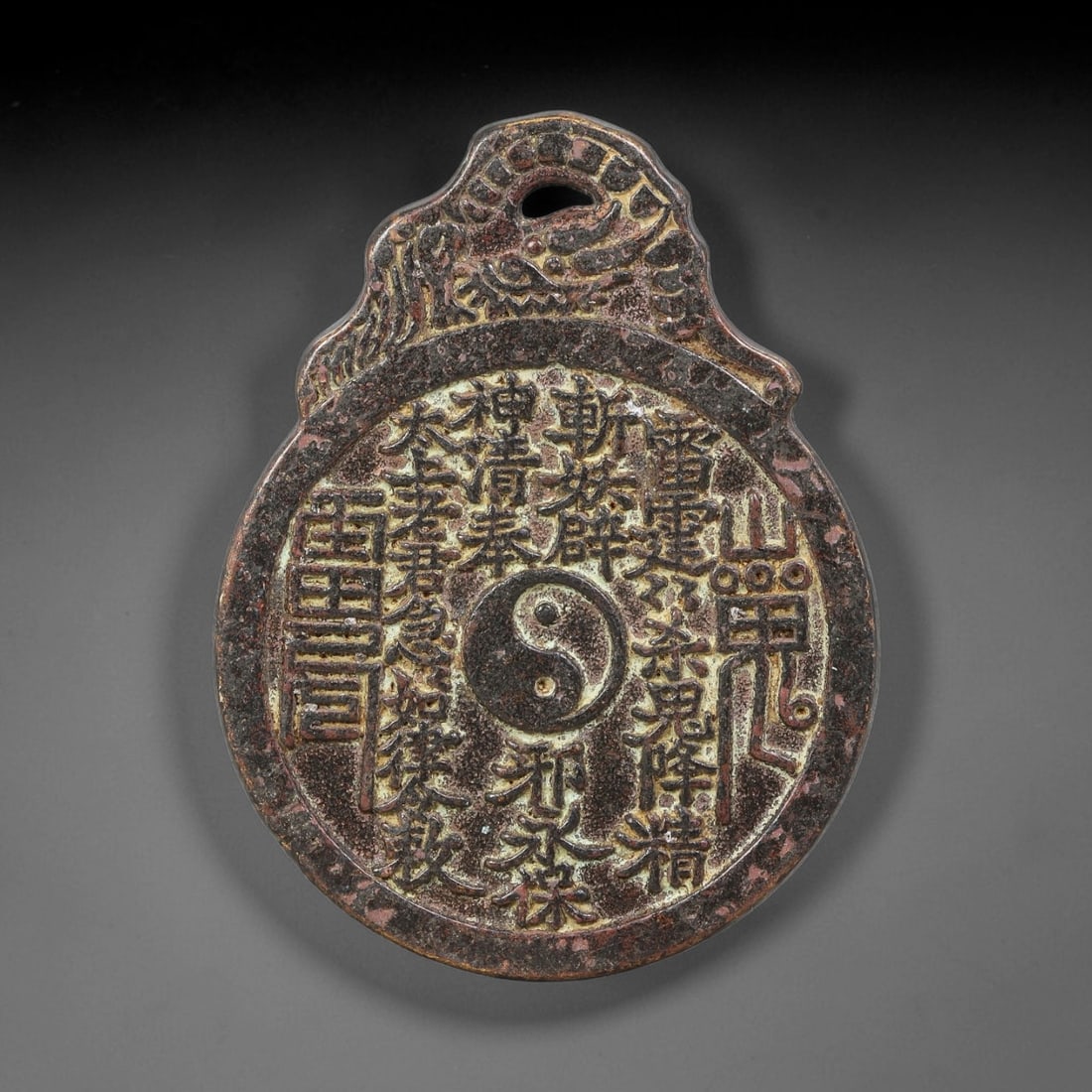 A Chinese Bronze Taoist Chant & Bagua Hanging Charm Amulet, 41AD: Cast bronze hanging amulet with ornate pierced suspension bail adorned with dragon-style relief detailing. Obverse features central yin-yang symbol surrounded by raised Taoist protective incantation t