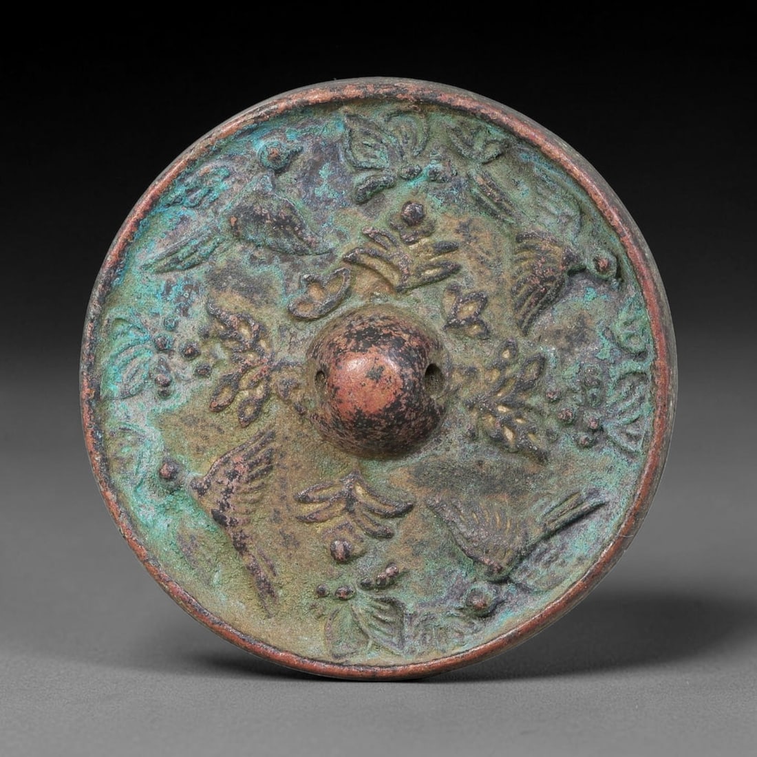 A Chinese Small Bronze Bird and Floral Motif Mirror, 49AD: Cast circular bronze mirror with prominent pierced central bulb boss. The surface is decorated in high relief with flying birds interspersed amongst blooming floral and foliate motifs arranged around 