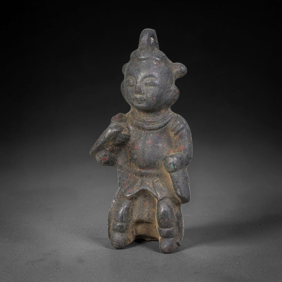 A Chinese Bronze Seated Attendant Figurine with Suspension Loop, 48AD: Cast bronze seated attendant figurine with an integral suspension loop moulded at the top of its headdress. The figure bears stylized facial features and structured layered garments, holding objects i