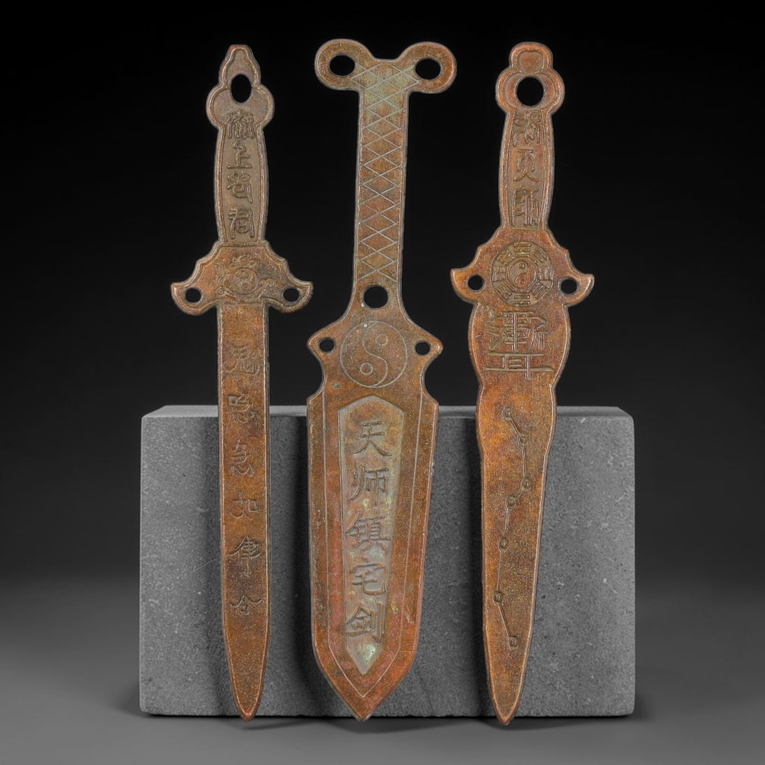 Lot of Three Chinese Bronze Taoist Ritual Sword Amulets, 35AD: Cast in bronze, this group of three flat ritual sword-form talismans each features suspension apertures for hanging. Their surfaces are finely engraved with Taoist iconography including yin-yang taiji