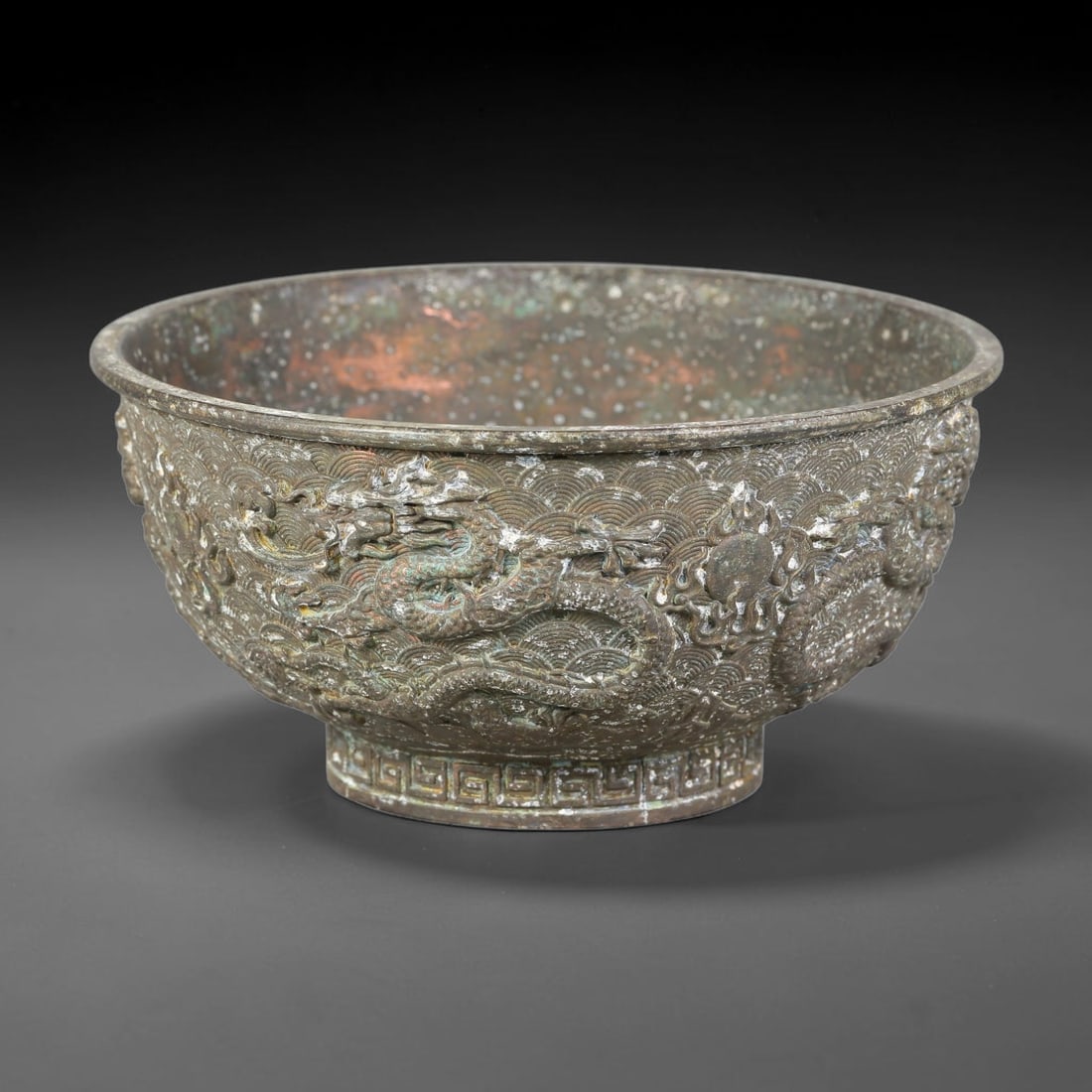 A Chinese Bronze Relief-Decorated Dragon Bowl, 22AJ: Cast bronze bowl with wide flared rim, rounded body and short stepped foot ring. The exterior is richly decorated in high relief with twin dragons chasing a flaming pearl amidst rolling wave patterns,
