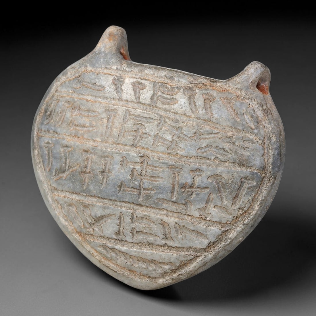 Ancient Uruk Period Hard-Stone Circular Inscribed Apotropaic Amulet (c.3500-3100 BCE), 64AJ: Circular-form apotropaic amulet of the Uruk cultural tradition, fitted with dual integrated suspension lugs at the upper margin for personal wear. Its face bears multiple horizontal registers of incis