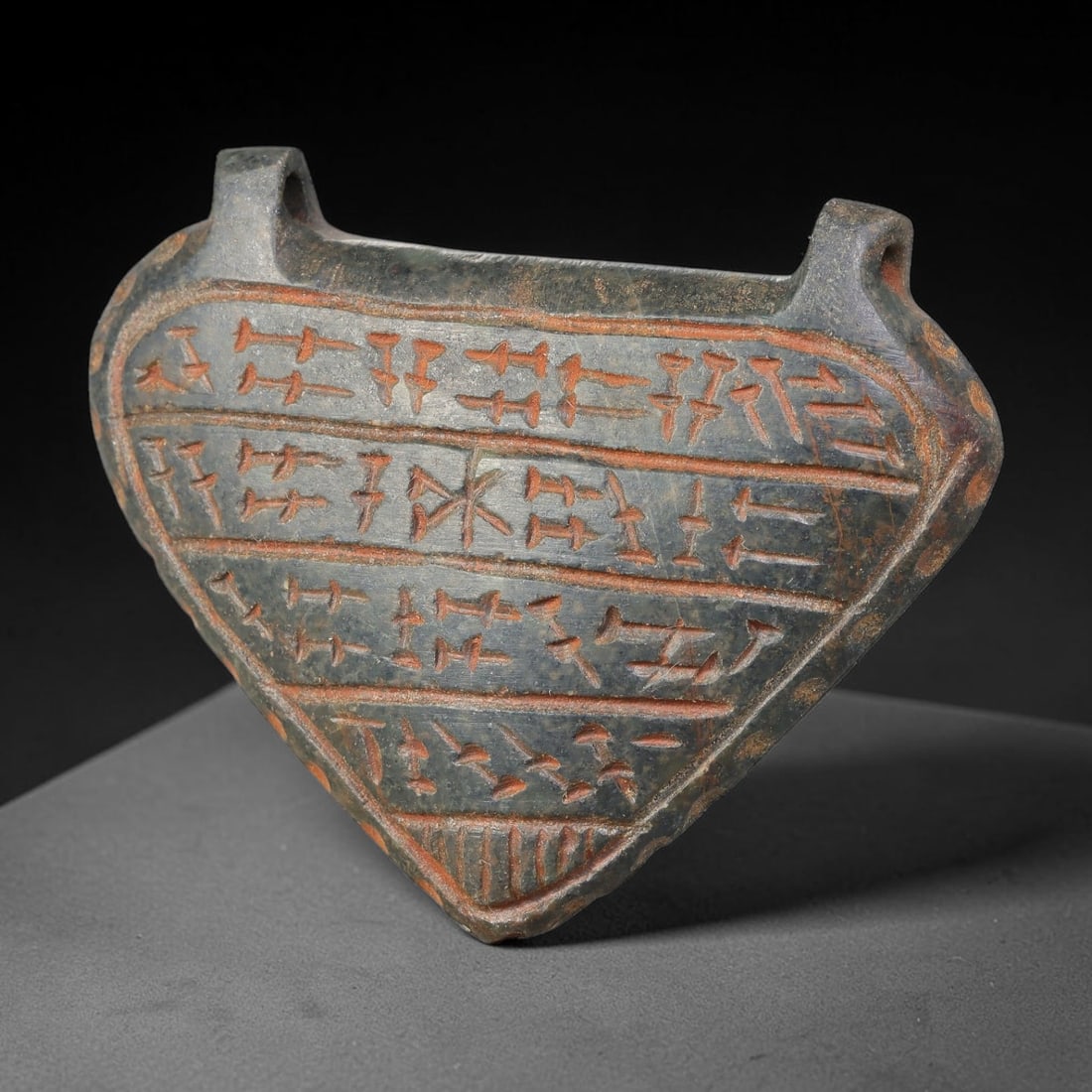 Ancient Uruk Period Hard-Stone Heart-Shaped Inscribed Apotropaic Amulet (c.3500-3100 BCE), 65AJ: Heart-form apotropaic amulet originating from the Uruk cultural sphere, featuring multiple horizontal registers of incised archaic symbolic script running across its surface. Two suspension lugs are i