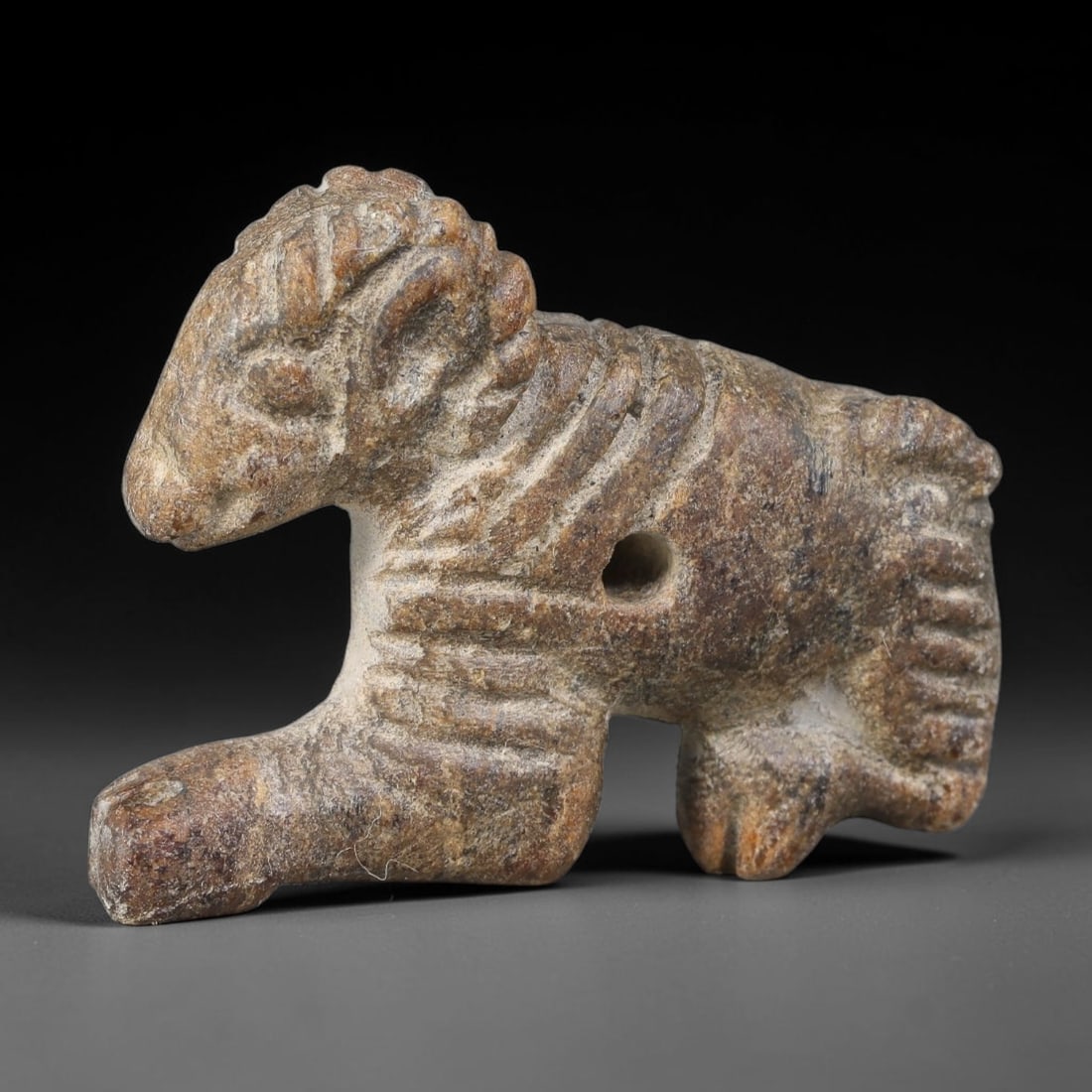 Ancient Sasanian Persian Hard-Stone Recumbent Ram Talisman Amulet (224-651 CE), 53AJ: Carved hard-stone apotropaic amulet depicting a recumbent ram, a well-documented zoomorphic motif within Sasanian Persian folk-ritual craft. Incised grooves render horn, mane and body textural element