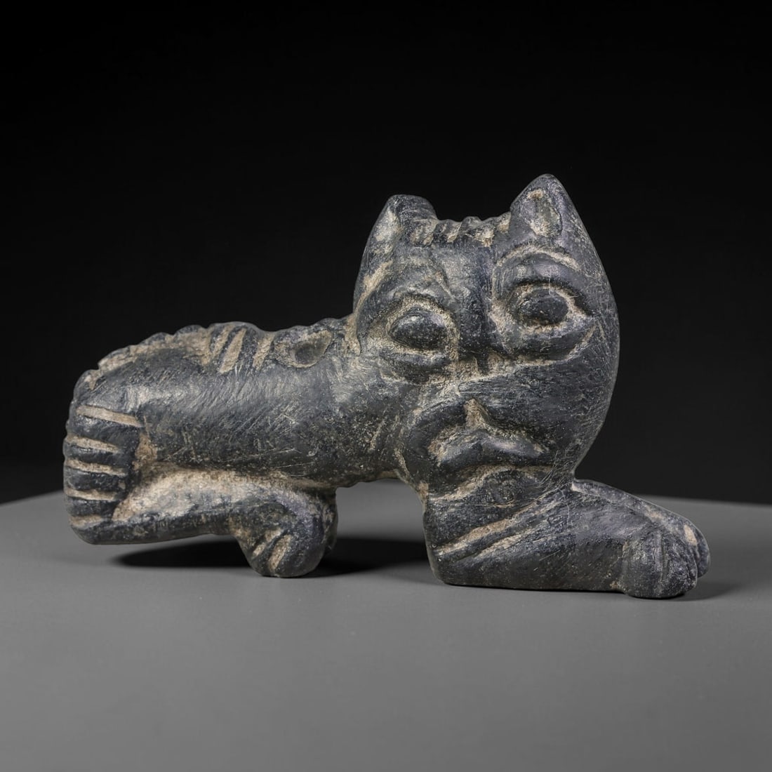 Ancient Sasanian Persian Schist Crouching Feline Apotropaic Talisman (224-651 CE), 50AJ: Dark schist carved crouching feline-form amulet executed in characteristic Sasanian Persian folk-ritual carving style. Distinct incised detailing defines facial features, mane and body patterning; a p