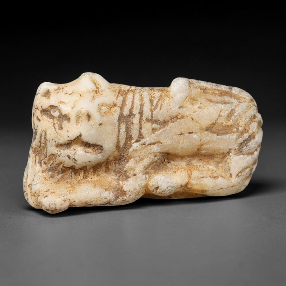 Ancient Sasanian Persian White Hard-Stone Recumbent Feline Talisman Amulet (224-651 CE), 54AJ: Carved white hard-stone amulet depicting a recumbent feline figure, a well-known protective motif within Sasanian Persian apotropaic craft. Incised lines render facial features, mane and body details.