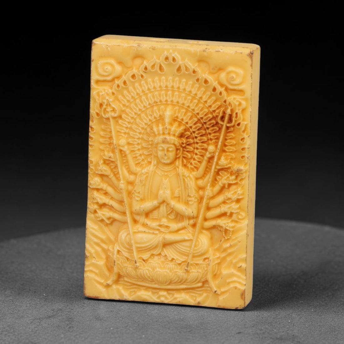 A Chinese Multi-Armed Guanyin Deity Carved Tagua Nut Pendant Amulet, 95BC: Carved from tagua nut, this rectangular tablet-form amulet is rendered in high relief. The multi-armed Guanyin sits in lotus position atop a detailed lotus base, central hands joined in anjali mudra a