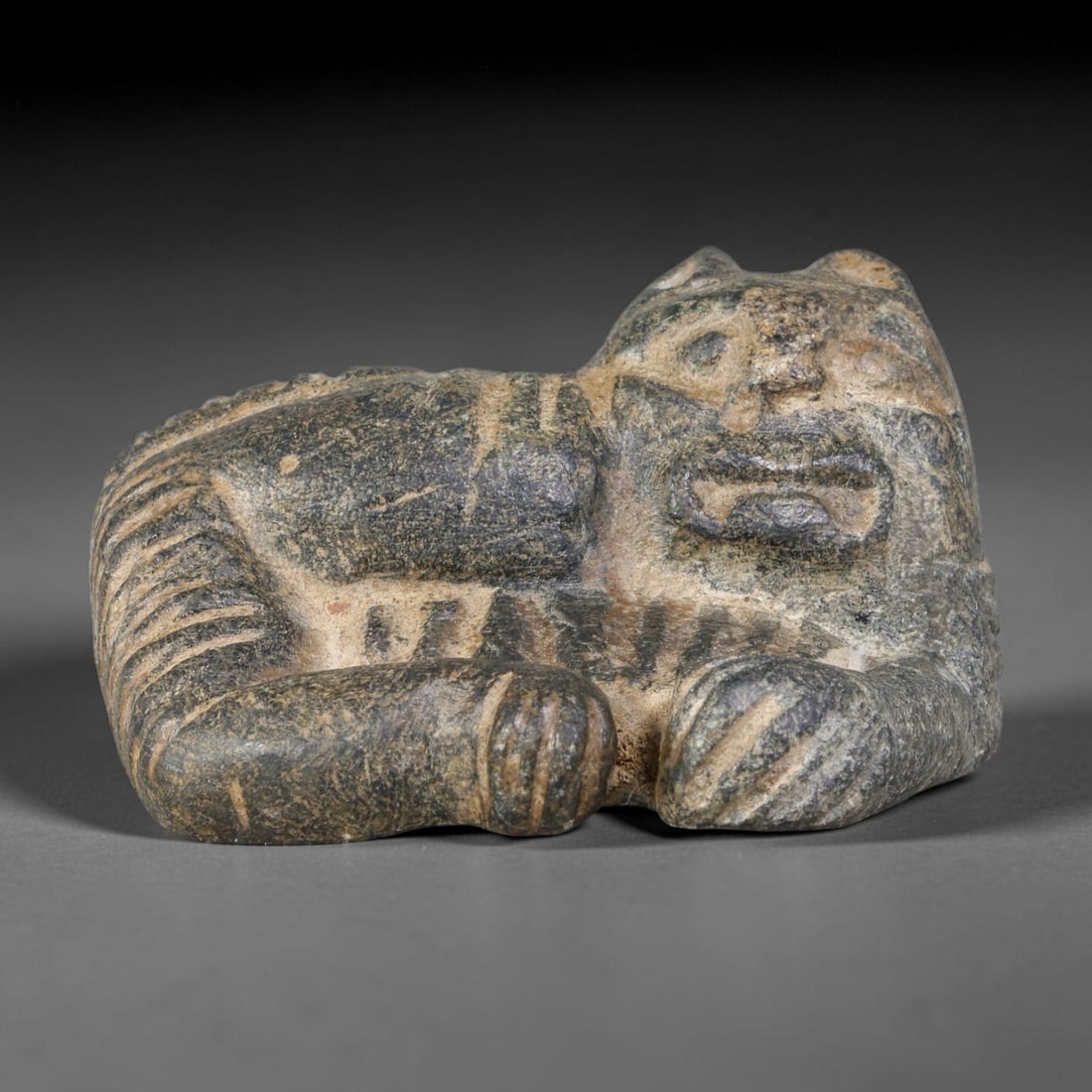 Ancient Sasanian Persian Schist Recumbent Feline Amulet (224-651 CE), 45AJ: Talismanic schist stone carving representing a recumbent feline creature, executed in Sasanian Persian sculptural idiom. Bold deep incised lines render facial features, paws and striped tail, embodyin