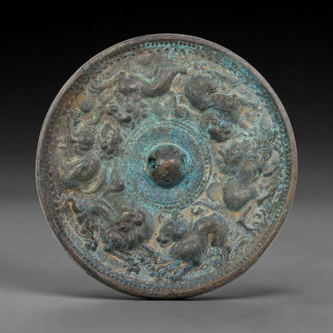 A Chinese Archaic-Style Bronze Mirror with Running Mythical Beasts Relief, 24AJ: Cast bronze circular mirror fitted with a central pierced hemispherical knob. The main field is decorated in relief with dynamically posed roaming mythical beasts arranged around the core, enclosed wi