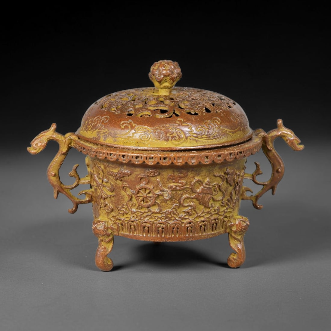 A Chinese Bronze Tripod Censer with Open-Work Lid and Buddhist Emblems, 96AD: Cast bronze tripod censer with pierced open-work domed lid surmounted by a floral-form finial for smoke dispersion. The cylindrical body is decorated in high relief with the eight Buddhist auspicious 