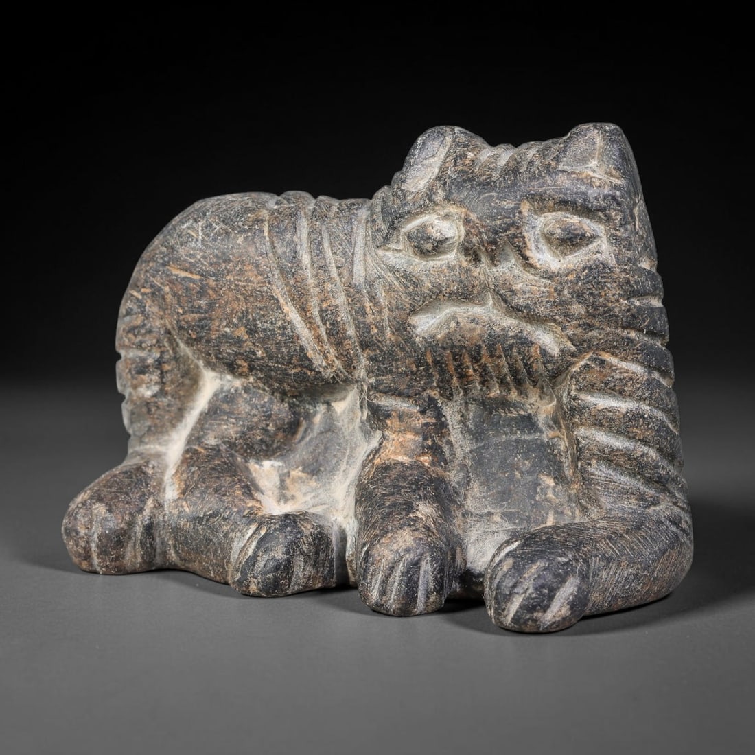 Ancient Sasanian Persian Schist Recumbent Feline Amulet (224-651 CE), 59AJ: Talismanic schist stone carving representing a recumbent feline creature, executed in Sasanian Persian sculptural idiom. Bold deep incised lines render facial features, paws and striped tail, embodyin