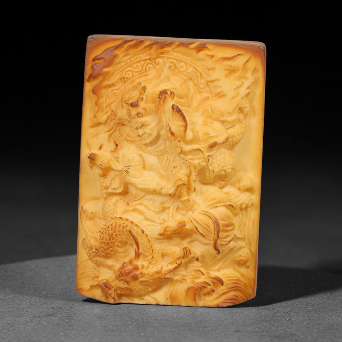 A Chinese Dragon Guardian Deity Carved Tagua Nut Pendant Amulet, 84BC: Carved from tagua nut, this rectangular tablet-form amulet is executed in deep high-relief carving. A fierce guardian deity is depicted in dynamic pose amid coiled dragon figures and turbulent wave mo