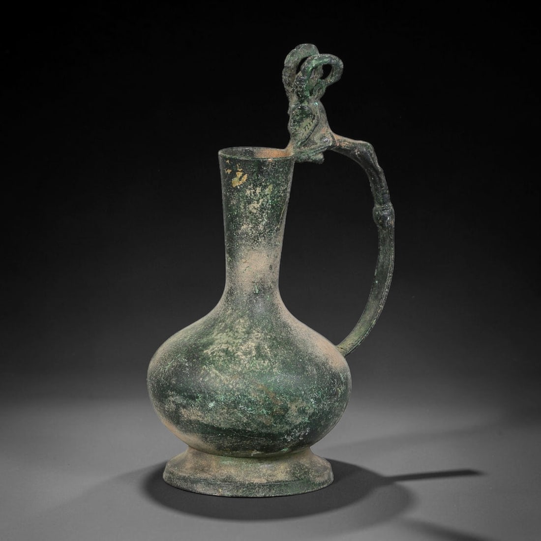 Ancient Seljuk Period Bronze Ewer (c.11th-12th Century CE), 97AK: This ancient Seljuk bronze ewer features a stylized figural finial forming the upper terminal of its curved handle, with a plain bulbous body, tall slender neck and flared foot base. The surface bears