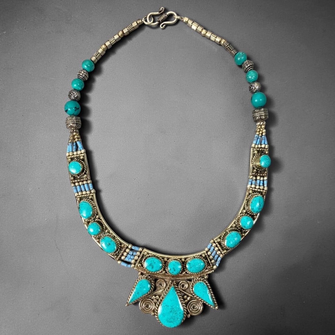 A Central Asian Multi-Metal Turquoise Inlaid Necklace, 3AL: Multi-metal necklace featuring spherical turquoise beads and textured tubular metal links forming the upper chain. Curved frontal panels hold multiple bezel-set turquoise cabochons, bordered by fine t