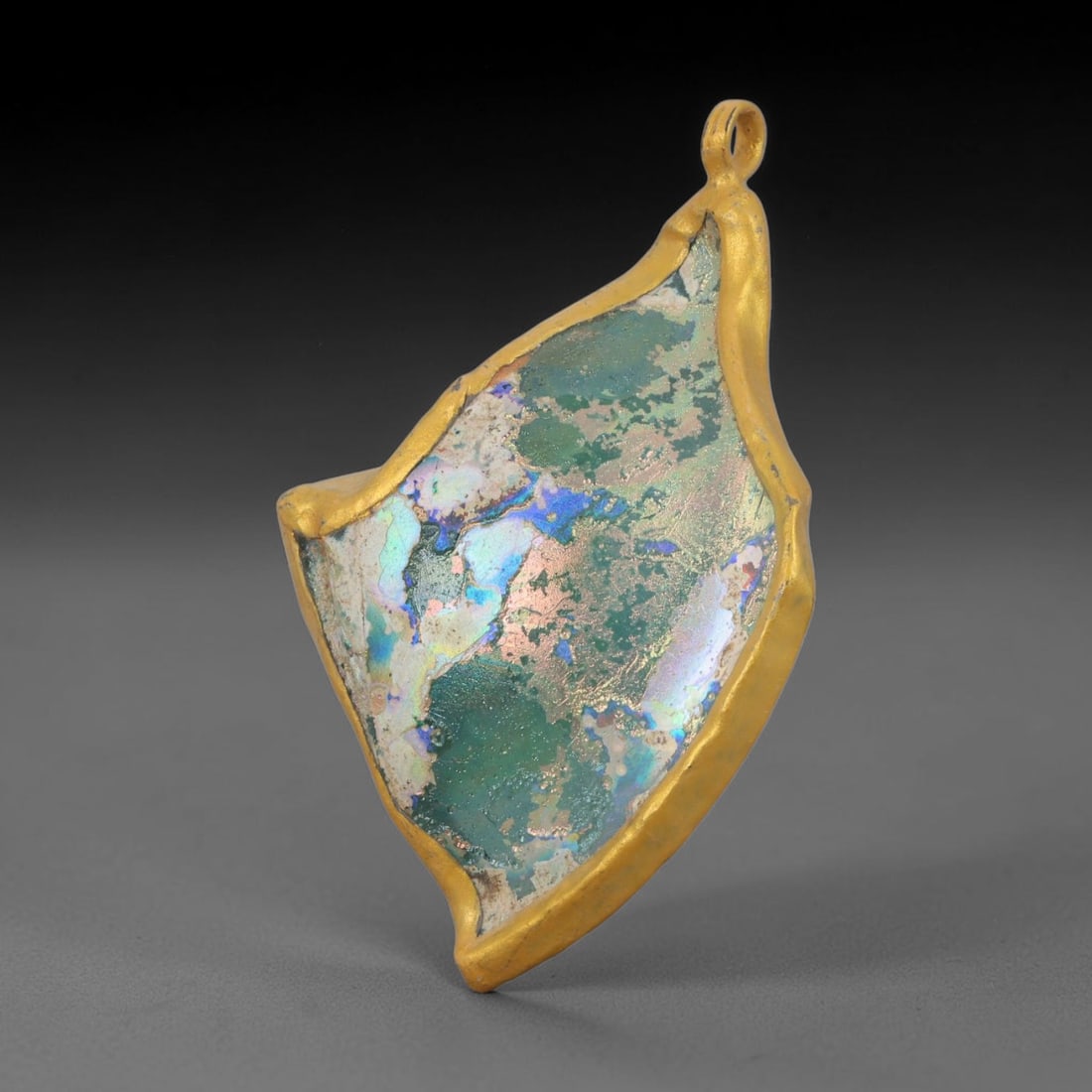 Ancient Roman Glass Slag in Modern Gilt-Edge Pendant, 56AK: This contemporary pendant is crafted from ancient Roman glass slag, featuring a fragmented, iridescent glass surface with weathered patina. The irregular form is bordered by a subtle gilt frame, added
