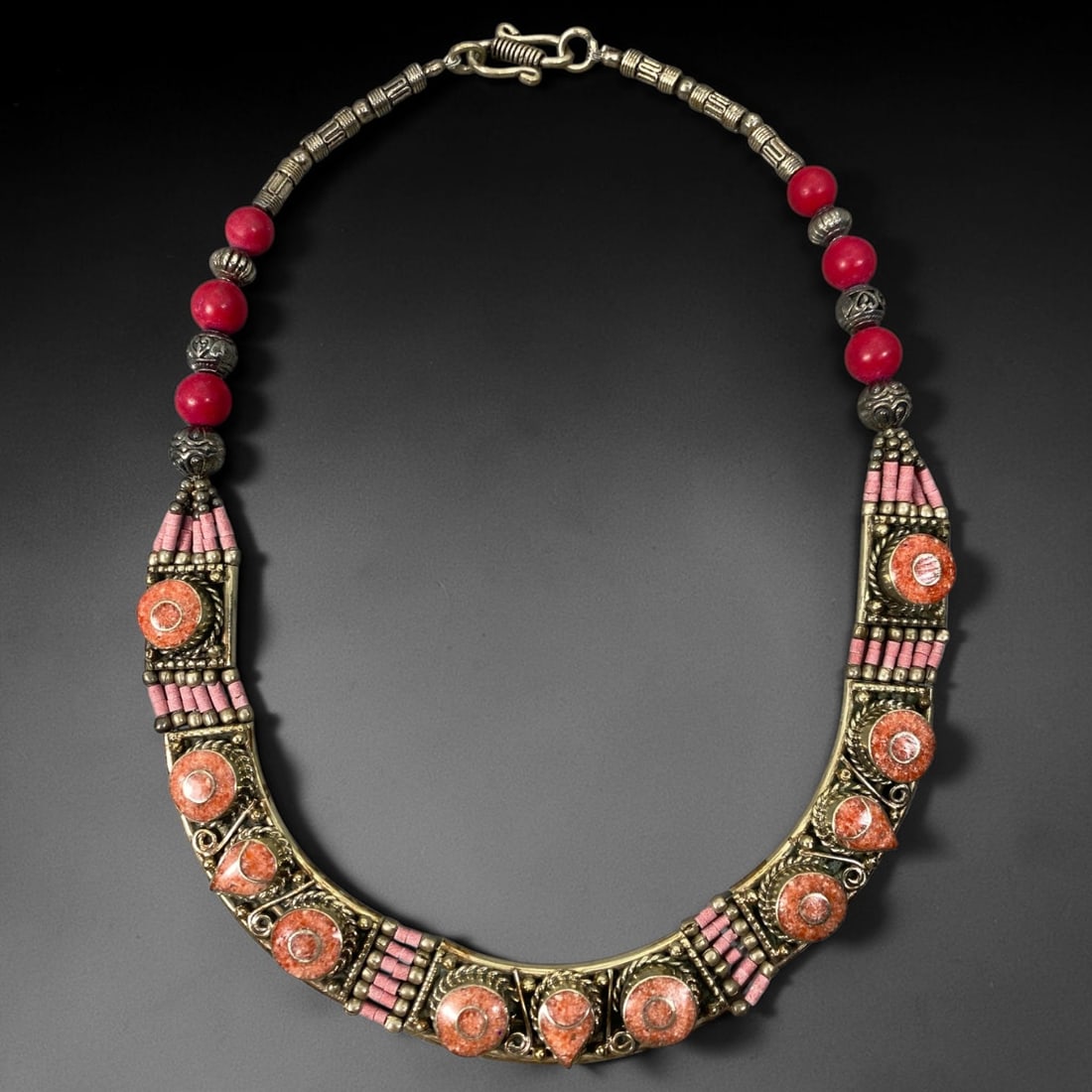 A Central Asian Multi-Metal Coral Composite Inlaid Necklace, 2AL: Multi-metal necklace constructed with spherical red beads and embossed textured metal beads along the upper chain. Curved frontal panels hold multiple circular and teardrop-shaped composite inlays wit
