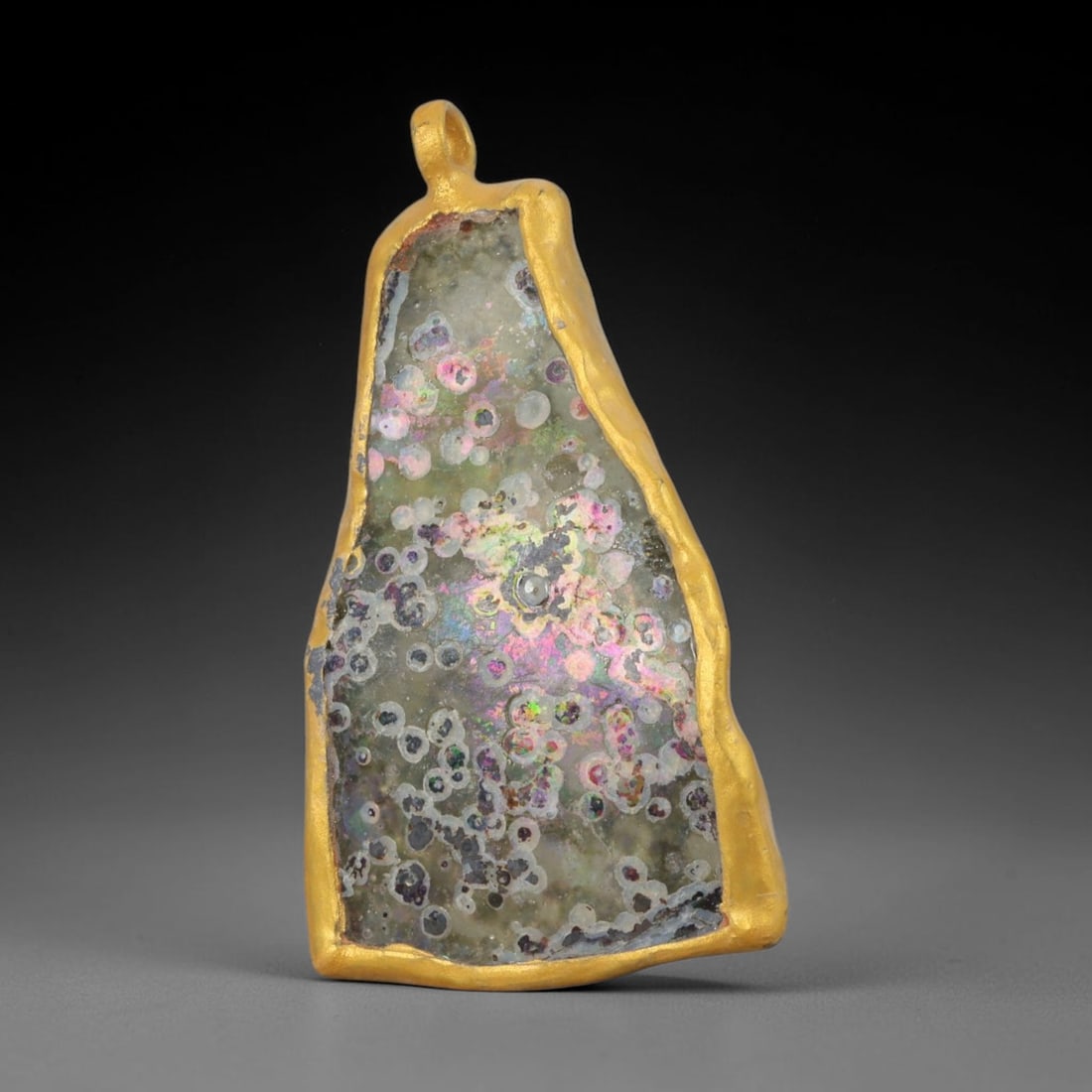 Ancient Roman Glass Slag in Modern Gilt-Edge Pendant, 58AK: This contemporary pendant is crafted from ancient Roman glass slag, featuring a fragmented, iridescent glass surface with weathered patina. The irregular form is bordered by a subtle gilt frame, added