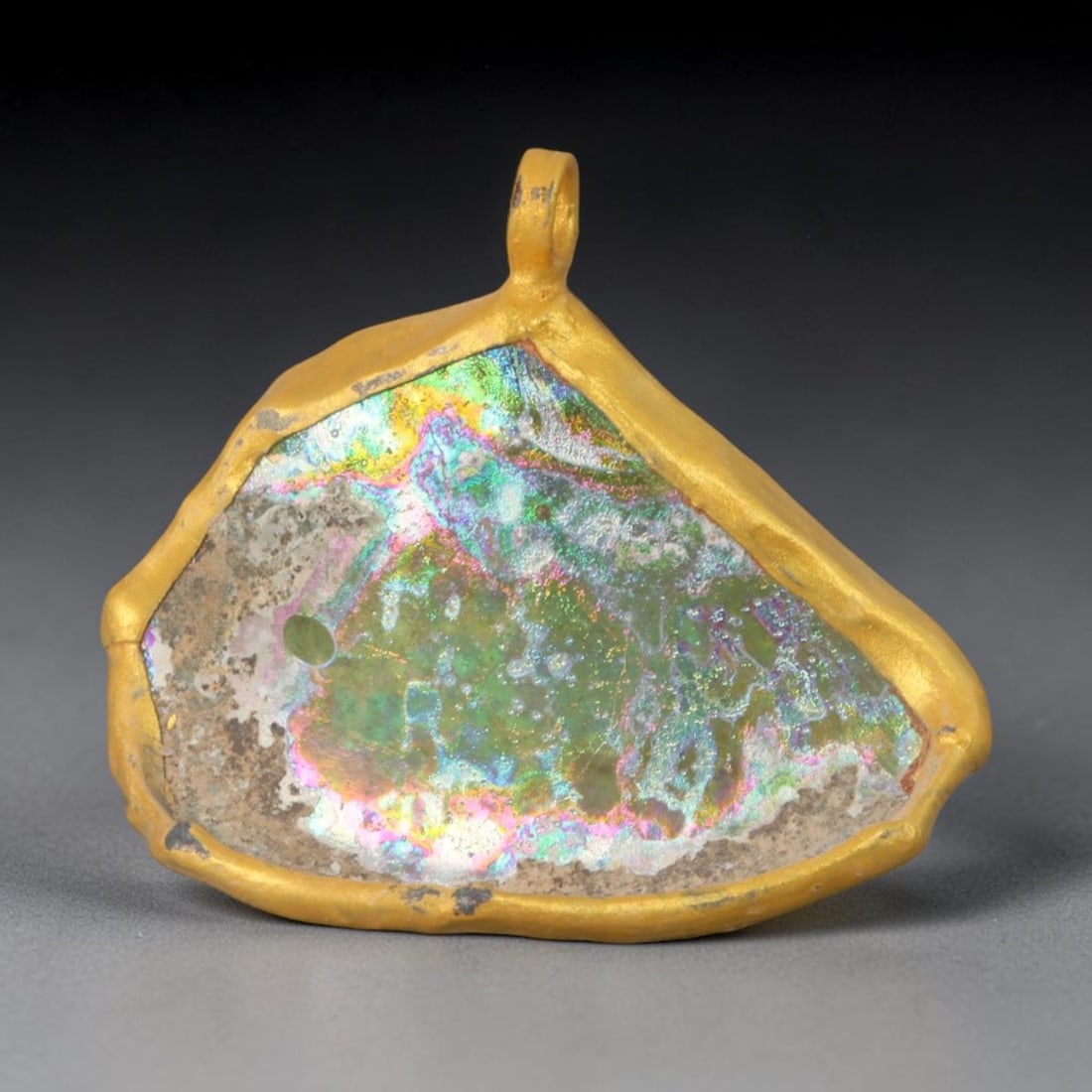 Ancient Roman Glass Slag in Modern Gilt-Edge Pendant, 54AK: This contemporary pendant is crafted from ancient Roman glass slag, featuring a fragmented, iridescent glass surface with weathered patina. The irregular form is bordered by a subtle gilt frame, added