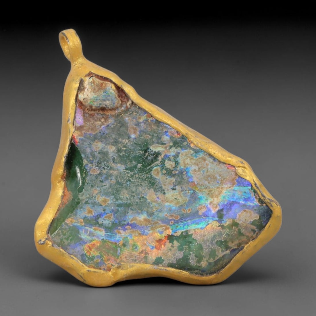 Ancient Roman Glass Slag in Modern Gilt-Edge Pendant, 59AK: This contemporary pendant is crafted from ancient Roman glass slag, featuring a fragmented, iridescent glass surface with weathered patina. The irregular form is bordered by a subtle gilt frame, added