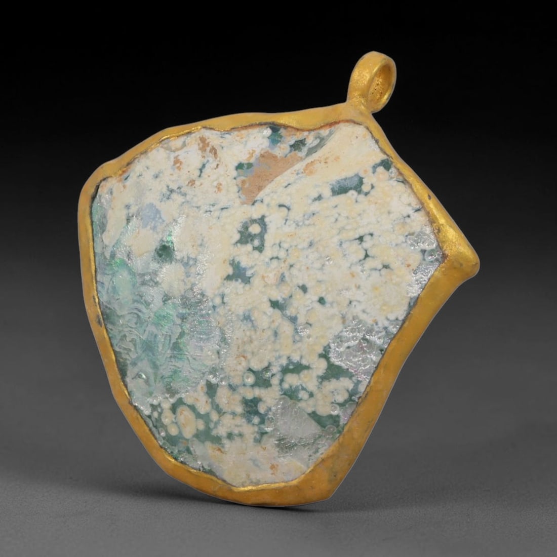 Ancient Roman Glass Slag in Modern Gilt-Edge Pendant, 55AK: This contemporary pendant is crafted from ancient Roman glass slag, featuring a fragmented, iridescent glass surface with weathered patina. The irregular form is bordered by a subtle gilt frame, added