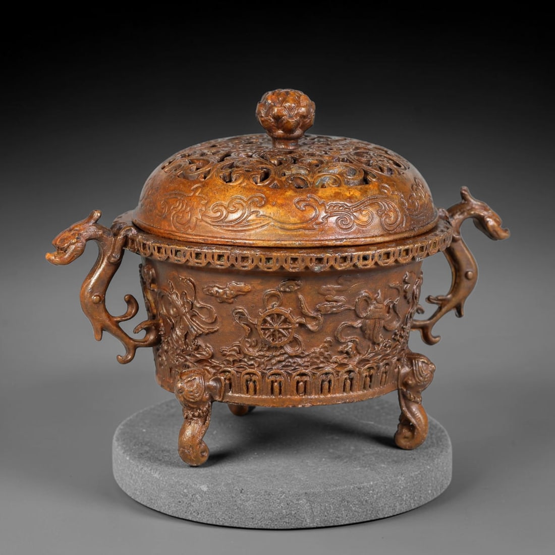 A Chinese Bronze Tripod Censer with Auspicious Buddhist Symbols and Dragon-Form Handles, 95AD: Cast bronze tripod censer fitted with a domed open-work lid surmounted by a full lotus-blossom finial, the lid surface decorated with scrolling cloud-relief motifs. The cylindrical body is cast in hig