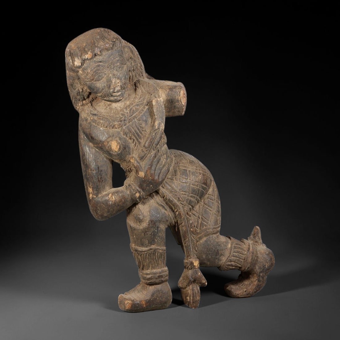 Antique Indo-Pacific Wood Deity Figure Figurine, 100AK: Carved wood figurine rendered in a dynamic leaning pose, with detailed facial features, stylised hair, carved neck adornment and patterned lower garment. The figure retains carved footwear and ankle o