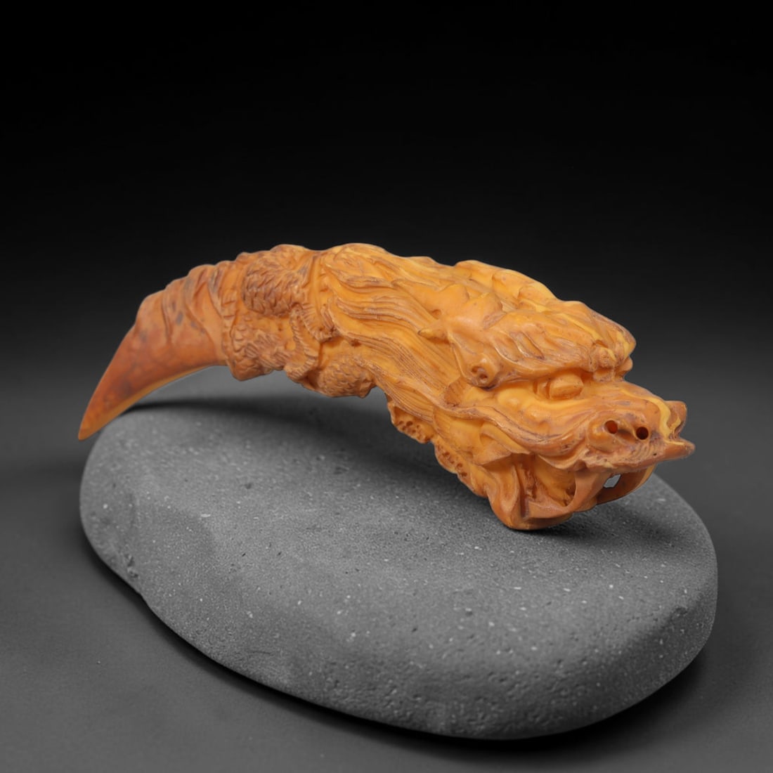 A Chinese Dragon Form Carved Tagua Nut Pendant Amulet, 12AD: Carved from tagua nut, this curved talon-shaped amulet is worked in high relief with a full dragon figure winding along the length of the object. The dragon head occupies the broader terminal, featuri