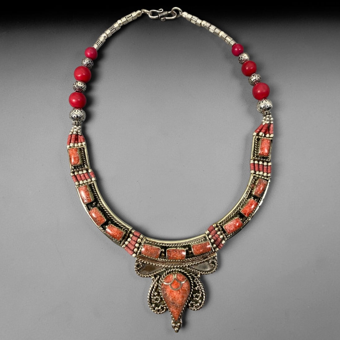 A Central Asian Multi-Metal Coral Composite Inlaid Necklace, 1AL: Multi-metal necklace assembled with large spherical red beads and engraved tubular metal links forming the upper chain. The curved collar-style front features multiple rectangular composite inlays set