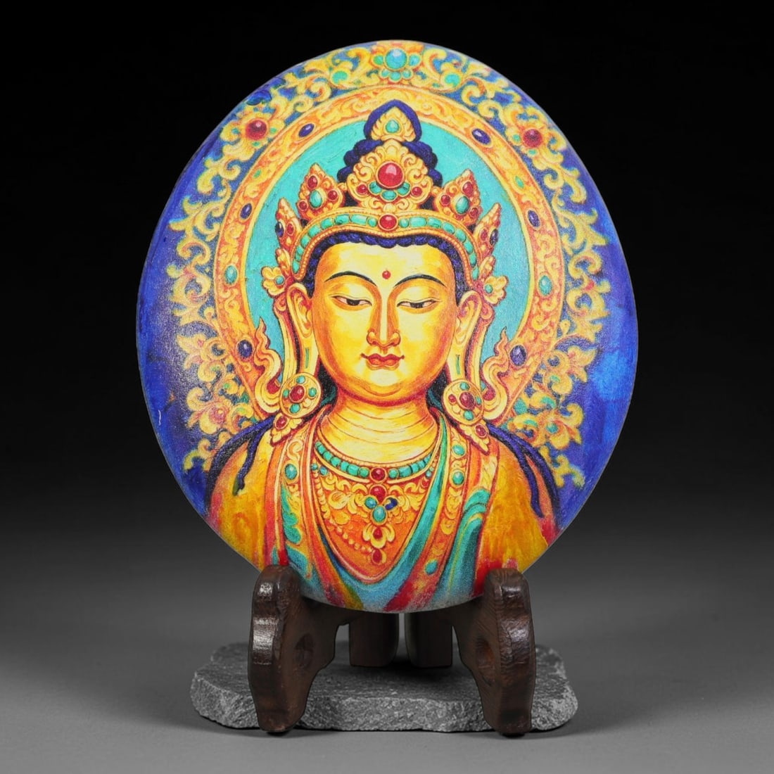 A Tibetan Thangka Style Painted River Stone with a Bodhisattva Figure, 69BC: Painted on a naturally rounded river stone with a smooth surface, the work depicts a bodhisattva figure in a thangka-style composition. The figure is shown with a serene countenance, an elaborate jewe