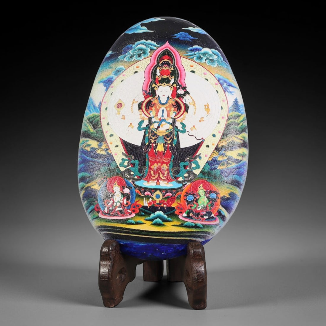A Tibetan Thangka Style Painted River Stone with a Thousand-Armed Avalokiteshvara, 61BC: Painted on a naturally rounded, egg-shaped river stone, the work depicts a thousand-armed Avalokiteshvara in a thangka-style composition. The central deity is shown with a complex and richly adorned f