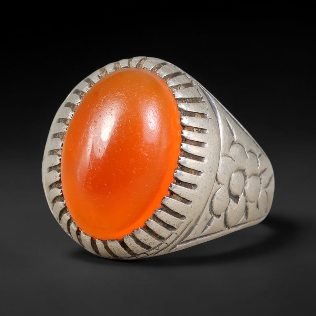 Antique Ottoman Carnelian Radiating Incised Bezel Floral Engraved Silver Ring, 19AL: Silver ring of the Ottoman period set with an oval cabochon carnelian secured within a radiating incised bezel. The ring shoulders carry detailed floral engraved decoration. No hallmarks present. Ring