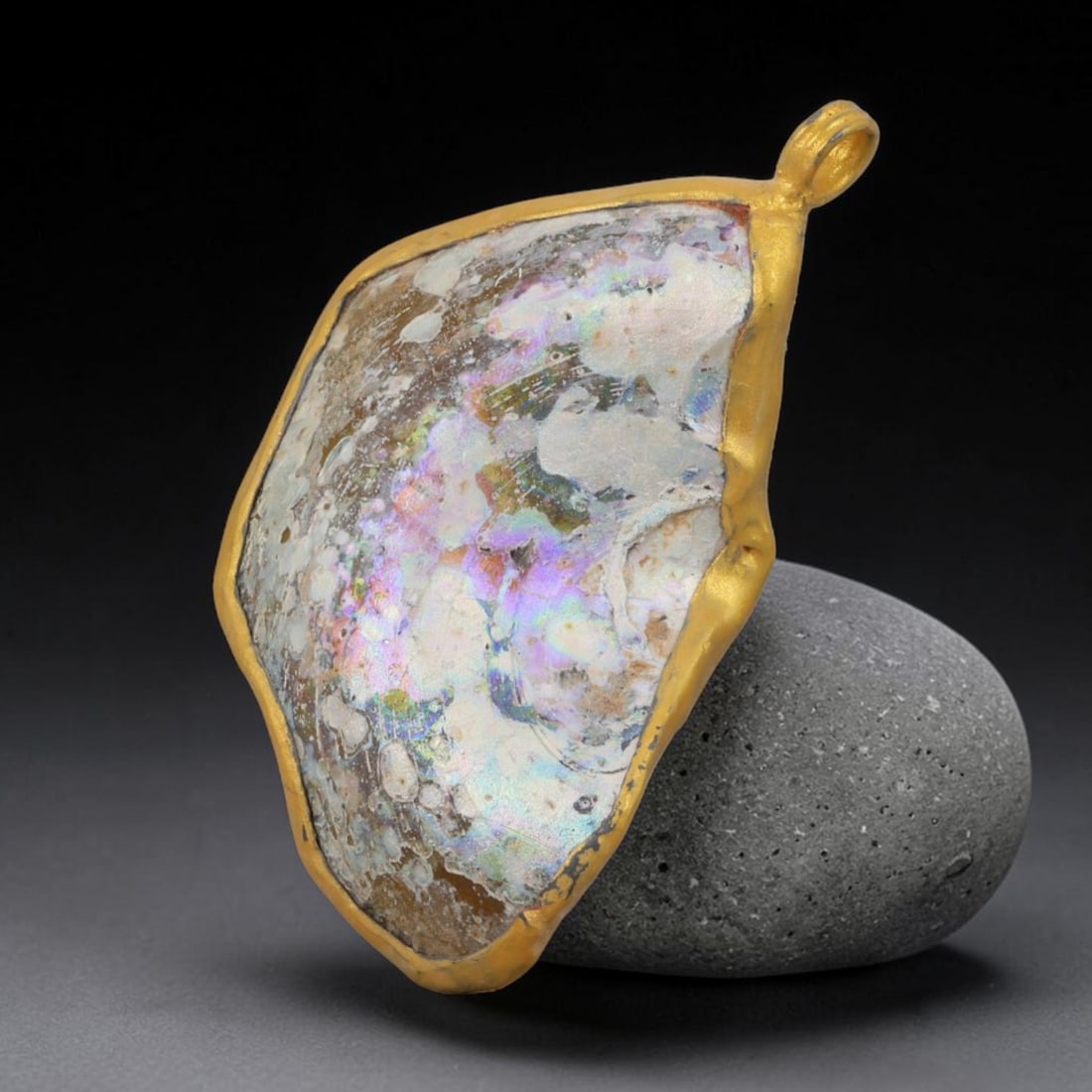 Ancient Roman Glass Slag in Modern Gilt-Edge Pendant, 61AK: This contemporary pendant is crafted from ancient Roman glass slag, featuring a fragmented, iridescent glass surface with weathered patina. The irregular form is bordered by a subtle gilt frame, added