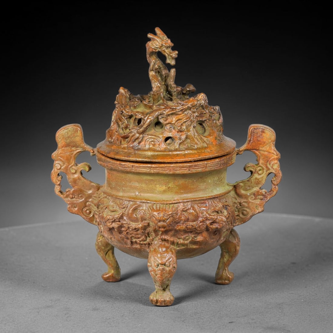 A Chinese Bronze Tripod Censer with Dragon-Finial Open-Work Lid, 94AD: Cast bronze tripod censer topped by an elaborately pierced open-work lid crowned with a coiled dragon finial. The bulbous body is richly cast in high relief with dragons amidst billowing cloud pattern