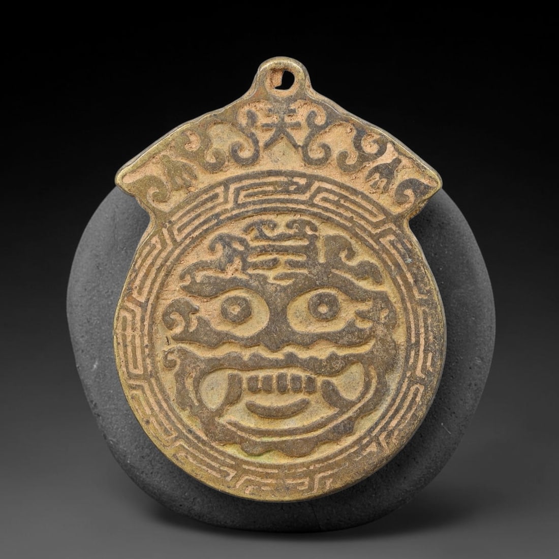 A Chinese Bronze Taotie-Face Bagua Protective Amulet Plaque, 46AD: Cast bronze hanging amulet plaque with pierced suspension loop at the ornate crown-style top. The obverse features prominent high-relief taotie mythical beast mask enclosed within geometric border pat