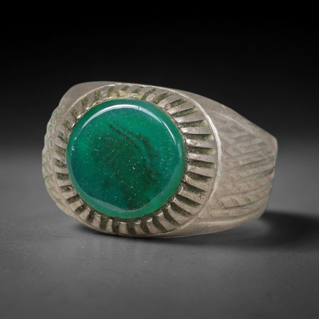Antique Ottoman Green Agate Radiating Incised Bezel Silver Ring, 21AL: Silver ring of the Ottoman period set with a round cabochon green agate secured within a radiating incised bezel. The wide shank carries fine linear engraved detailing. No hallmarks present. Ring size