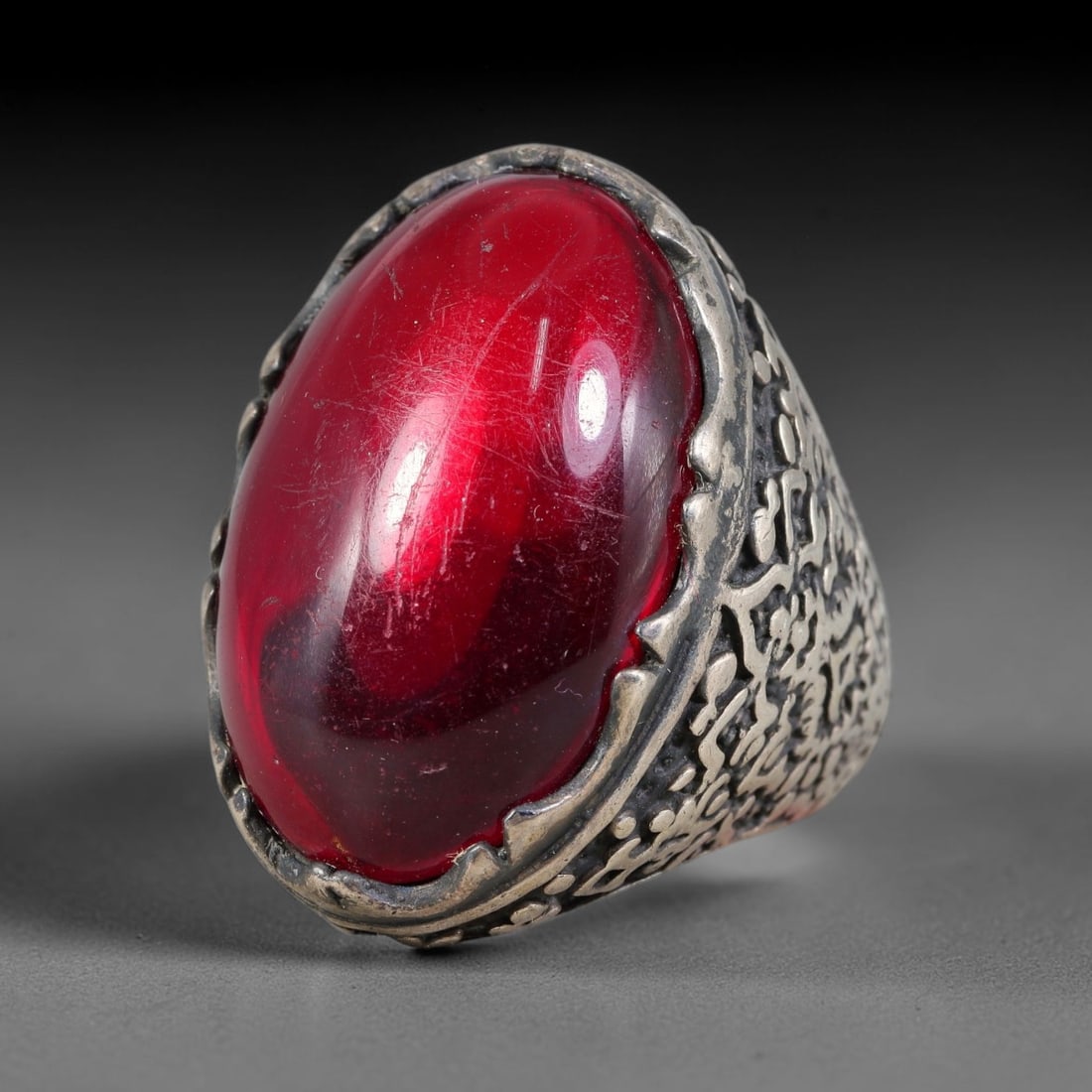 Antique Ottoman Red Glass Engraved Silver Ring, 8AL: Silver ring of the Ottoman period set with a large oval cabochon red glass stone within a serrated bezel. The shoulders of the shank display dense engraved ornamentation, no calligraphy present. No ha
