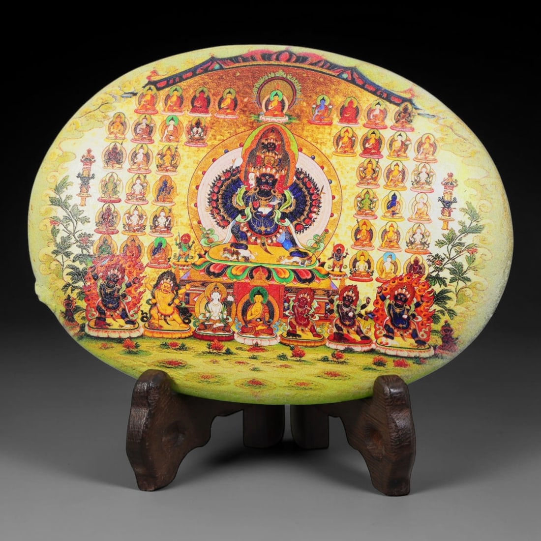 A Tibetan Thangka Style Painted River Stone with a Protective Deity, 80BC: Painted on a naturally rounded river stone, the work depicts a protective deity in a thangka-style composition. The central figure is shown with an imposing presence, surrounded by numerous smaller bu