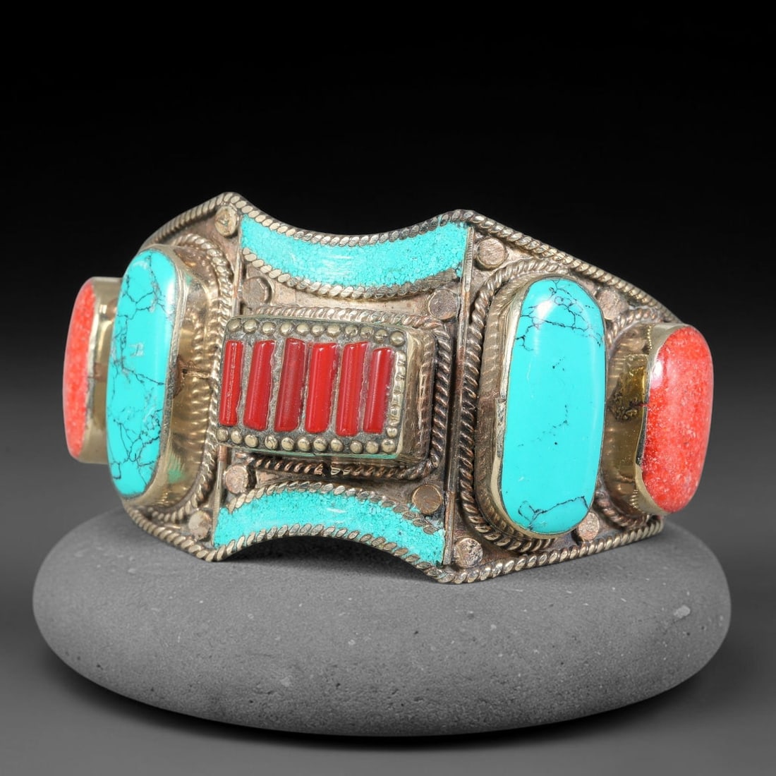 A Tibetan Copper-Alloy Turquoise and Red Inlay Cuff Bracelet, 45AK: Constructed from copper-alloy metal, this cuff bracelet features multiple set inlay elements. The mounting incorporates twisted wire and stud detailing across the surface. Internal diameter 8 cm, band