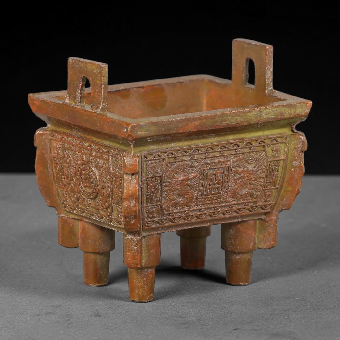 A Chinese Miniature Bronze Rectangular Ding Ritual Vessel, 18AJ: Cast bronze miniature rectangular ding vessel with two upright pierced rectangular handles, standing upon eight short cylindrical legs. Each of the four exterior faces bears finely engraved relief pan